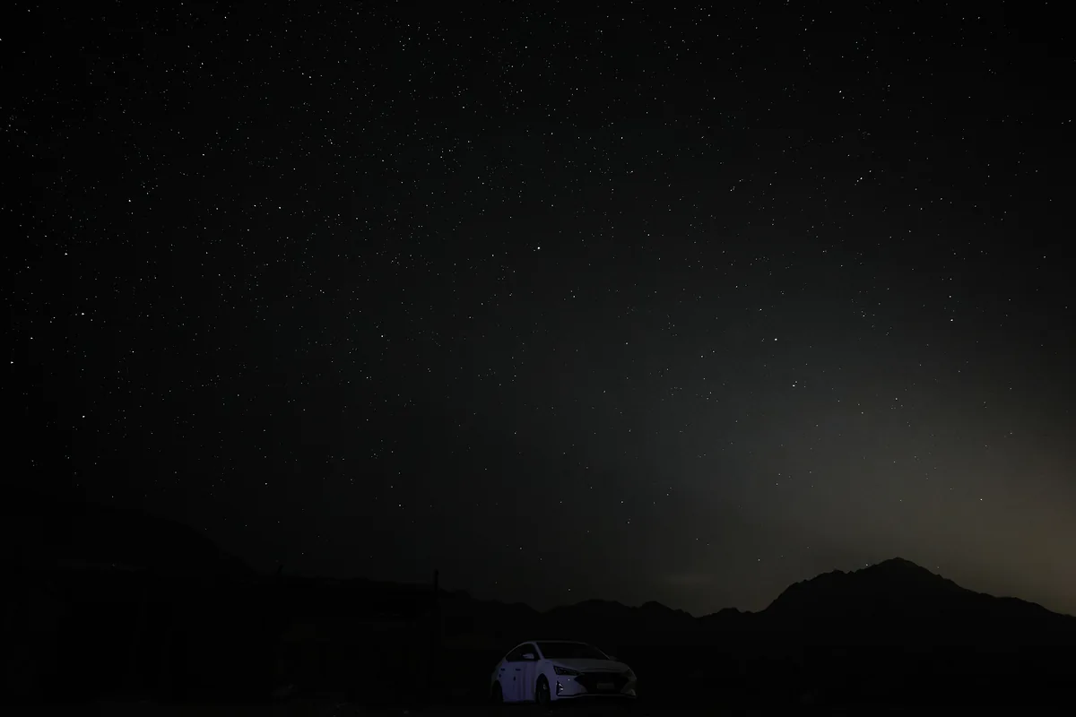 Lone car under a vast dark starry sky